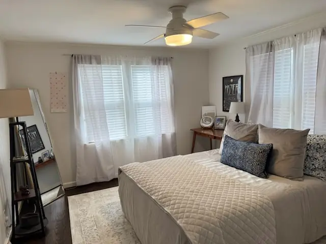 Made bed under a ceiling fan in a bright bedroom with white shutters